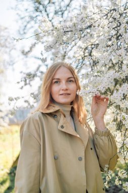 Çiçek açan bahar bahçesinde kokunun tadını çıkaran genç bir kadının portresi. Seyahat, özgürlük ve bahar tatili.