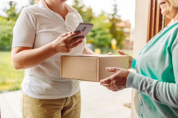 Close up of an young woman is receiving a parcel from mailman delivered in her home. Concept of courier, delivery, e-commerce, online shopping — Photo