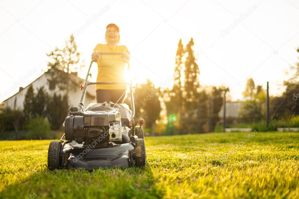 Portrait of beautiful 50s senor woman cutting grass with gasoline lawn mower, gardening