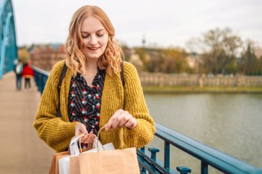 Mutlu gülümseyen 30 'lu yaşlardaki modaya uygun kıyafetler giyen, dışarıda kağıt torbalarla poz veren ve içine bakan kadınlar. Bahar alışveriş konsepti