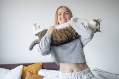 Spor ev kıyafetleri içindeki kadın elleri evde büyük bir tekir kediyi tutuyor. Duygularını ifade eden arkadaşlar