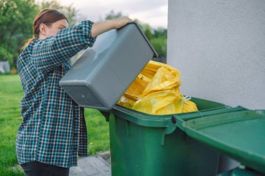 30 'lu yaşlardaki güzel Avrupalı bir kadın evin yakınındaki arka bahçedeki çöp kutusuna çöp atıyor.