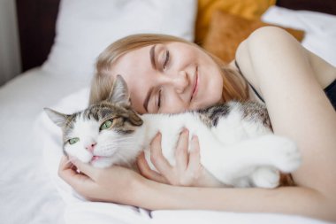 Kadın, evdeki yatakta ellerinin arasında kediye sarılıyor. Evde kal. Kendine dikkat et. Aşk, bakım, evlat edinme