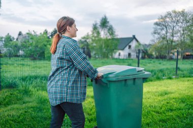 Plastik kirliliği sorunu. Avrupalı 20 'li yaşlarda bir kız çöpü bir evin yakınındaki çöp kutusuna atıyor. Çöpleri çöp kutularına koy. Gönüllüler ve sorumlu toplum.