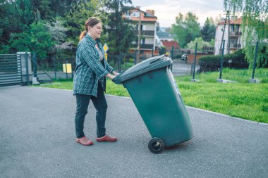 Plastik kirliliği sorunu. Avrupalı 20 'li yaşlarda bir kız çöpü bir evin yakınındaki çöp kutusuna atıyor. Çöpleri çöp kutularına koy. Gönüllüler ve sorumlu toplum.