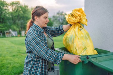 30 'lu yaşlardaki güzel Avrupalı bir kadın evin yakınındaki arka bahçedeki çöp kutusuna çöp atıyor.