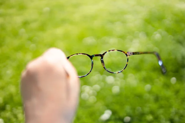 Woman with poor eyesight. Poor eyesight, hand holding stylish frame glasses on a green blurred background