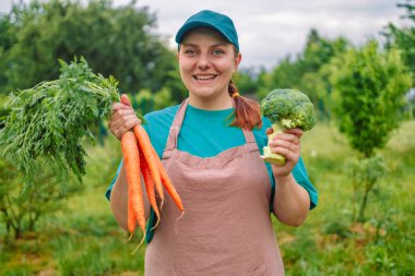 Bahçede bir demet eko havuç ve yeşil brokoli ile kadın çiftçiye yakın çekim. 