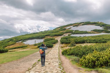 Dağın tepesinde sırt çantalı bir erkek yürüyüşçü. Spor giysili bir adam bir dağın fotoğrafını çekiyor. Babia Gora Polonya. 
