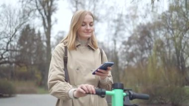 Kadın, park alanında elektrikli scooter ya da bisiklete biniyor, sokakta turist telefonu uygulaması kullanıyor. Şehirde çevre dostu ulaşım