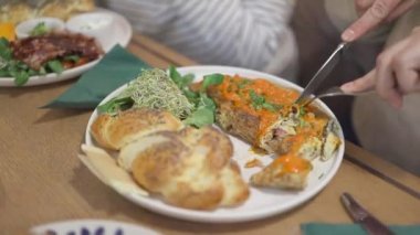 Caddedeki kafedeki ahşap masada omlet ve ıspanak yapraklarıyla sandviç kesen kadın videosu.