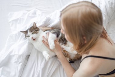 Kadın, evdeki yatakta ellerinin arasında kediye sarılıyor. Evde kal. Kendine dikkat et. Aşk, bakım, evlat edinme