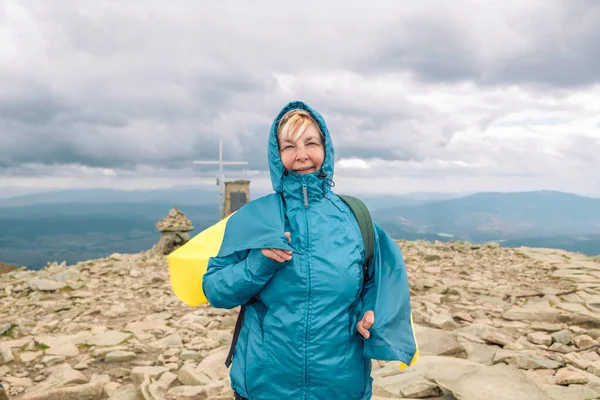 50s woman hiking with Ukraine flag at top of mountains with sports backpack. Travel adventure concept. Babia Gora Poland