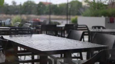 Arka planda sağanak yağmurda sokak restoranının siyah masaları ve sandalyeleri