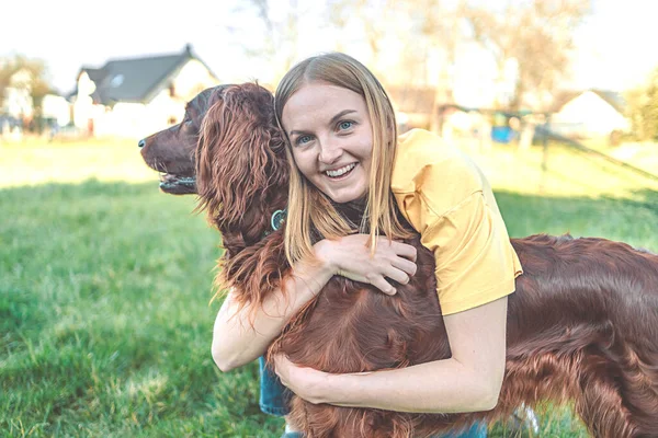 在公园里 女人在鲜绿色的草地上与她的红色爱尔兰猎犬玩耍 她高兴地微笑着 — 图库照片