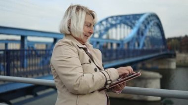 Olgun bir yetişkin stil kadın telefonu kullanır ve güneşli bir sonbahar gününde şehirde dolaşırken etrafına bakar.. 