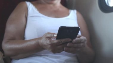 Senior woman travelling on train in daytime. Woman sitting near window, side view female using cell phone for messaging and communication. 4K