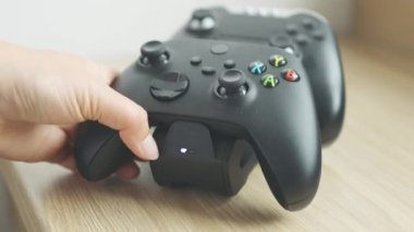 Play oyun kablosuz şarj aleti için iki siyah kumanda. Kadın eli, kumandanın şarj olmasını engelliyor. 4k