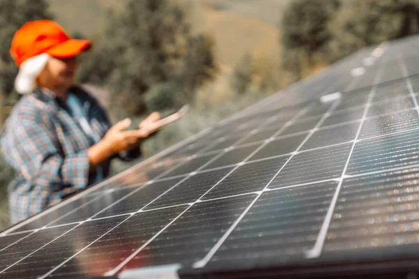 Senior engineer is checking with tablet an operation of sun and cleanliness on field of photovoltaic solar panels on a sunset. Renewable energy, technology, electricity, service concept 