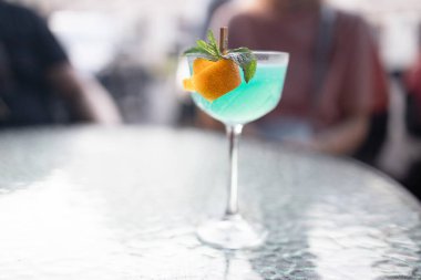 Glass of Blue Lagoon cocktail on light grey table, outdoors