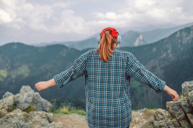 Bir kadın yolcunun kablosuz kulaklıklarla sakin müzikler dinlemesi dağın tepesinde tek başına durup harika bir atmosferin keyfini çıkarması.