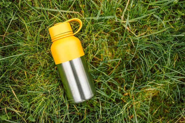 Water bottle. Reusable steel thermo water bottle on green grass. Steel thermo water bottle