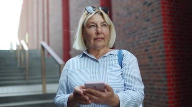 Avrupa 'da şehir caddesinde gözlüklü yaşlı bir kadın cep telefonuna bakıyor.