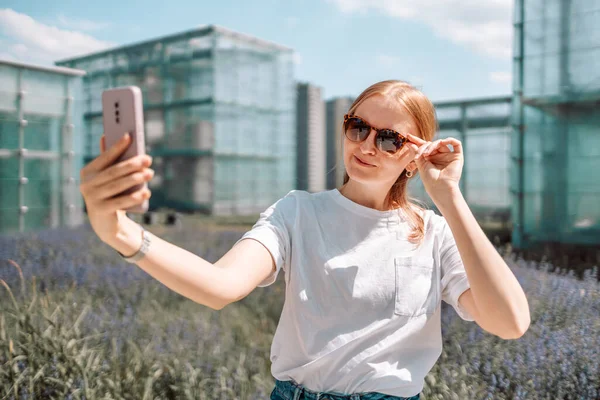 Happy blonde girl taking picture of herself while walking around town. Taking selfie self portrait photos on smartphone.