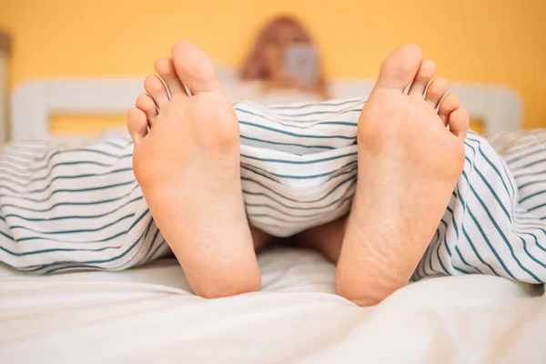 Woman feet on the bed under white blanket. Sleeping and relax concept. Vacation and Holiday theme. Beautiful feet of a young woman lying in bed close up.