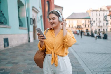 Mutlu beyaz kadın gündelik kıyafetlerini giyer müzik dinler ve telefon ekranına bakar. Pozitif duygu kavramı