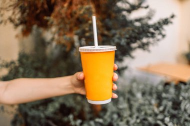 Kadın eli, şehir caddesinde tek kullanımlık bardakla ferahlatıcı bir yaz içkisi tutuyor. Tasarım için boş alan. Yüksek kalite fotoğraf