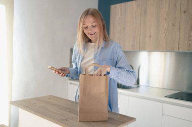 Yemek teslimatı konsepti. Göndermek için paket hazırlayan, akıllı telefon kullanan, teslimat servisi sipariş eden bir kadın.