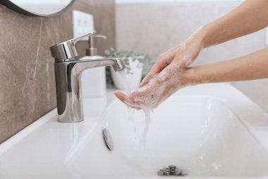 Akan su musluğunun altında ellerini yıkamak. Hijyen konsepti el detayı. Corona virüsünün önlenmesi için sabunla ellerini ovuşturmak, korona virüsünü halka yaymayı durdurmak için hijyen. Ya da umumi tuvalette.