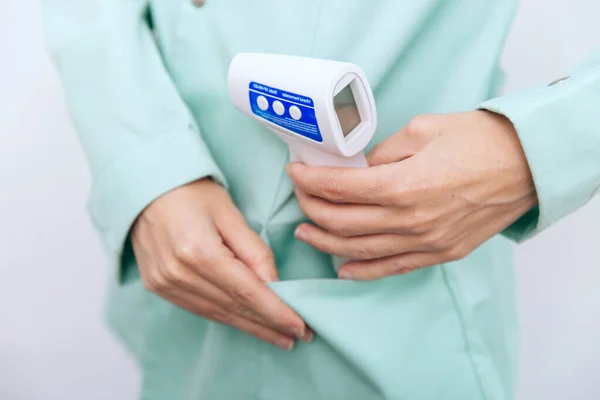 Temperature measurement gun in doctor hands. Close-up shot of doctor wearing protective surgical mask ready to use infrared isometric thermometer gun to check body temperature for virus symptoms — Stock Photo, Image