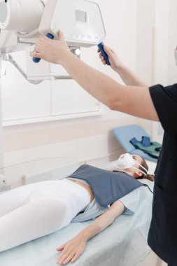 Doktor sedyede yatan hastanın röntgenini çekiyor. Hastane radyoloji odası. Teknisyen röntgen cihazını ayarlıyor. Yatakta yatan kadın modern klinikte göğüs, kalp ve akciğerleri tarıyor.