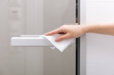 Cam kapı kollarını antiseptik ıslak mendille temizliyorum. Hastane ve kamusal alanlarda korona virüsüne karşı korunma yüzeylerini sterilize edin. Kadın eli temizlik için havlu kullanıyor.