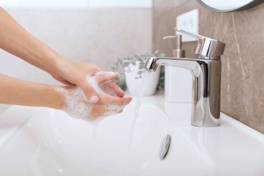 Akan su musluğunun altında ellerini yıkamak. Hijyen konsepti el detayı. Corona virüsünün önlenmesi için sabunla ellerini ovuşturmak, korona virüsünü halka yaymayı durdurmak için hijyen. Ya da umumi tuvalette.