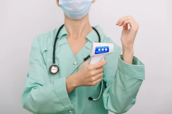 Temperatuurmeetpistool in doktershanden. Close-up shot van de arts met beschermende chirurgische masker klaar voor gebruik infrarood isometrische thermometer pistool om de lichaamstemperatuur te controleren op virussymptomen — Stockfoto