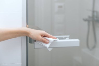 Cam kapı kollarını antiseptik ıslak mendille temizliyorum. Hastane ve kamusal alanlarda korona virüsüne karşı korunma yüzeylerini sterilize edin. Kadın eli temizlik için havlu kullanıyor.