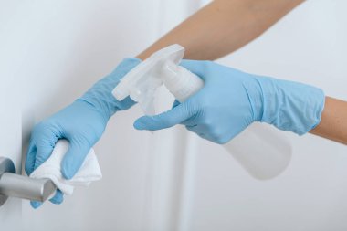 Antiseptik ıslak mendil, mavi eldiven ve dezenfektanla siyah kapı kolunu temizliyorum. Hastane ve kamusal alanlarda korona virüsüne karşı korunma yüzeylerini sterilize edin. Kadın eli temizlik için havlu kullanıyor.