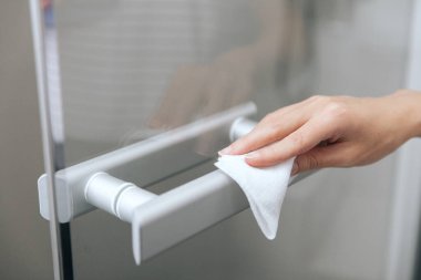 Cam kapı kollarını antiseptik ıslak mendille temizliyorum. Hastane ve kamusal alanlarda korona virüsüne karşı korunma yüzeylerini sterilize edin. Kadın eli temizlik için havlu kullanıyor.
