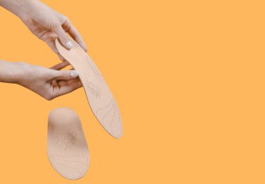 Turuncu bir arka planda ortopedik insole izole edildi. Tıbbi tabanlar. Düz taban ve ayak hastalıklarının tedavisi ve önlenmesi. Ayak bakımı, ayak rahatlığı. Rahat ayakkabılar giy. Düz Ayak Düzeltme
