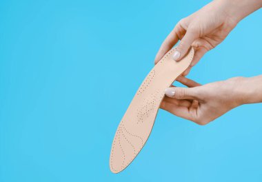 Mavi bir arkaplanda ortopedik insole izole edildi. Tıbbi tabanlar. Düz taban ve ayak hastalıklarının tedavisi ve önlenmesi. Ayak bakımı, ayak rahatlığı. Rahat ayakkabılar giy. Düz Ayak Düzeltme