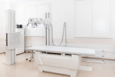 Modern hastanenin röntgen bölümü. Boş yataklı tarama makineli radyoloji odası. Teknisyen röntgen cihazını ayarlıyor. Modern klinikte göğüs, kalp ve akciğerler taranıyor.