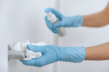 Antiseptik ıslak mendil, mavi eldiven ve dezenfektanla siyah kapı kolunu temizliyorum. Hastane ve kamusal alanlarda korona virüsüne karşı korunma yüzeylerini sterilize edin. Kadın eli temizlik için havlu kullanıyor.