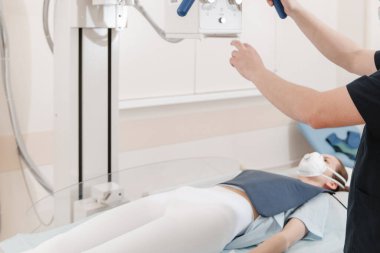 Doktor sedyede yatan hastanın röntgenini çekiyor. Hastane radyoloji odası. Teknisyen röntgen cihazını ayarlıyor. Yatakta yatan kadın modern klinikte göğüs, kalp ve akciğerleri tarıyor.