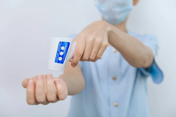 Temperature measurement gun in doctor hands. Close-up shot of doctor wearing protective surgical mask ready to use infrared isometric thermometer gun to check body temperature for virus symptoms — Stock Photo, Image