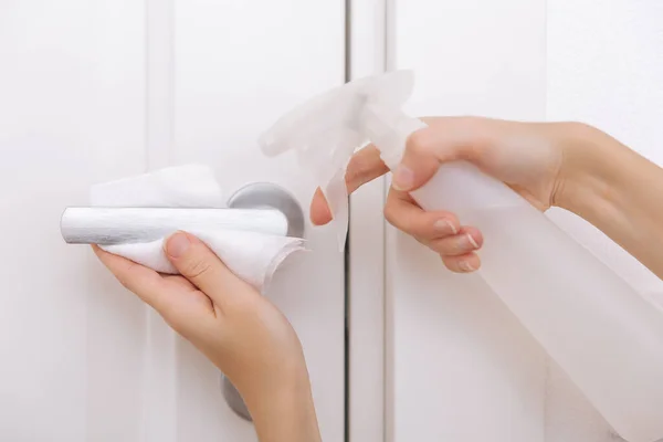 Cleaning white door handles with an antiseptic wet wipe and sanitizer spray. Disinfection in hospital and public spaces against corona virus. Woman hand using towel for cleaning home room door link