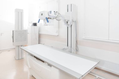 Modern hastanenin röntgen bölümü. Boş yataklı tarama makineli radyoloji odası. Teknisyen röntgen cihazını ayarlıyor. Modern klinikte göğüs, kalp ve akciğerler taranıyor.