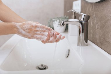 Akan su musluğunun altında ellerini yıkamak. Hijyen konsepti el detayı. Corona virüsünün önlenmesi için sabunla ellerini ovuşturmak, korona virüsünü halka yaymayı durdurmak için hijyen. Ya da umumi tuvalette.